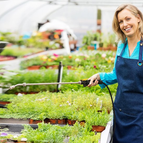femme qui utilise Lance pulverisateur pour les plantes dans une serre