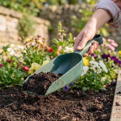 personne qui utilise Pelle verte pour apporté de la terre dans le carré de jardin 